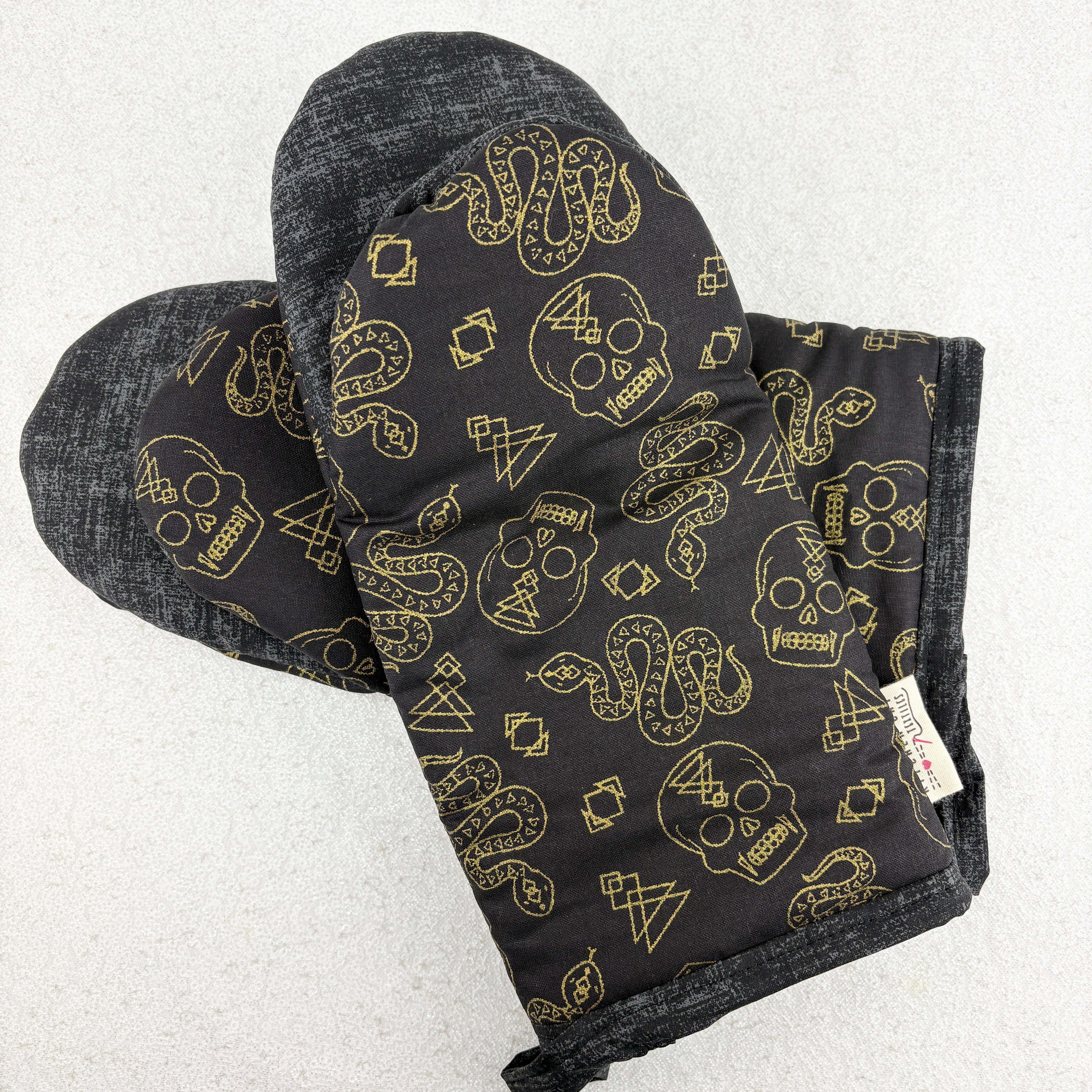Black oven mitt with gold skull and snake pattern on a white background