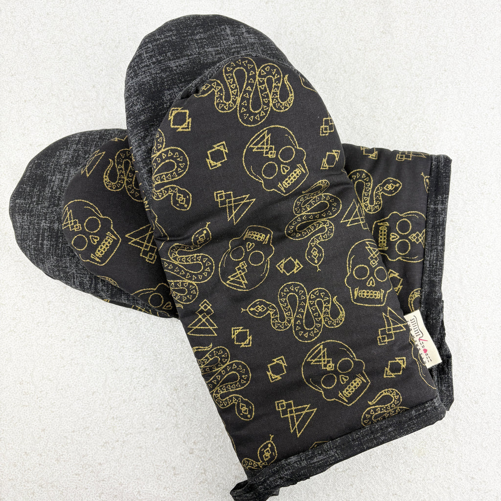 Black oven mitt with gold skull and snake pattern on a white background