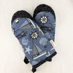 Load image into Gallery viewer, A pair of oven mitts featuring a blue and gray nautical-themed print with sailboats, seashells, starfish, and ship's wheels, finished with black patterned cuffs.
